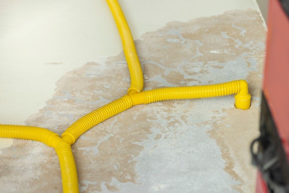 Yellow corrugated plastic tubing on a textured beige and gray surface, likely a wall.