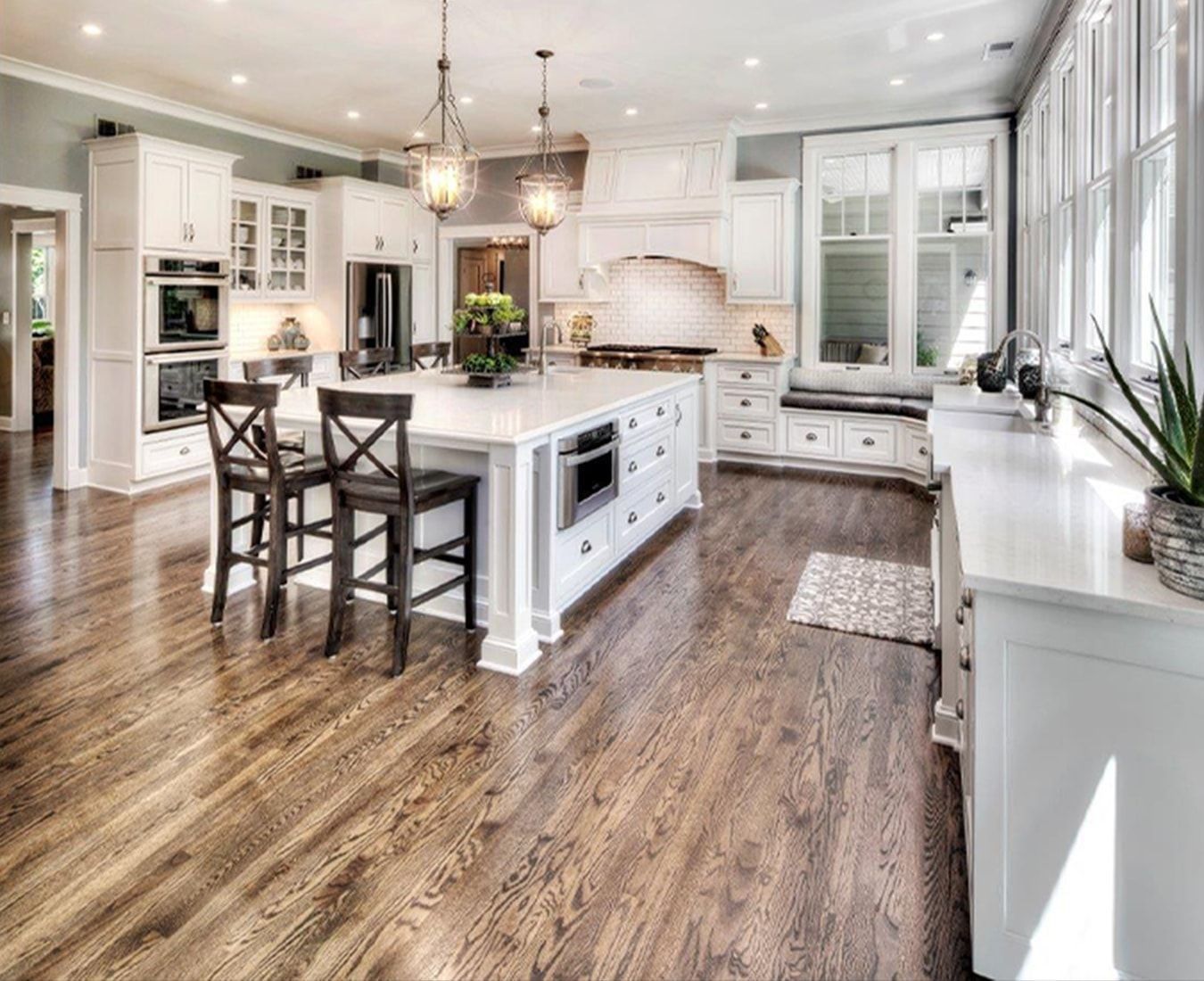Spacious kitchen with a large island, white cabinets, and dark wood floors. Sunlight streams through the windows.