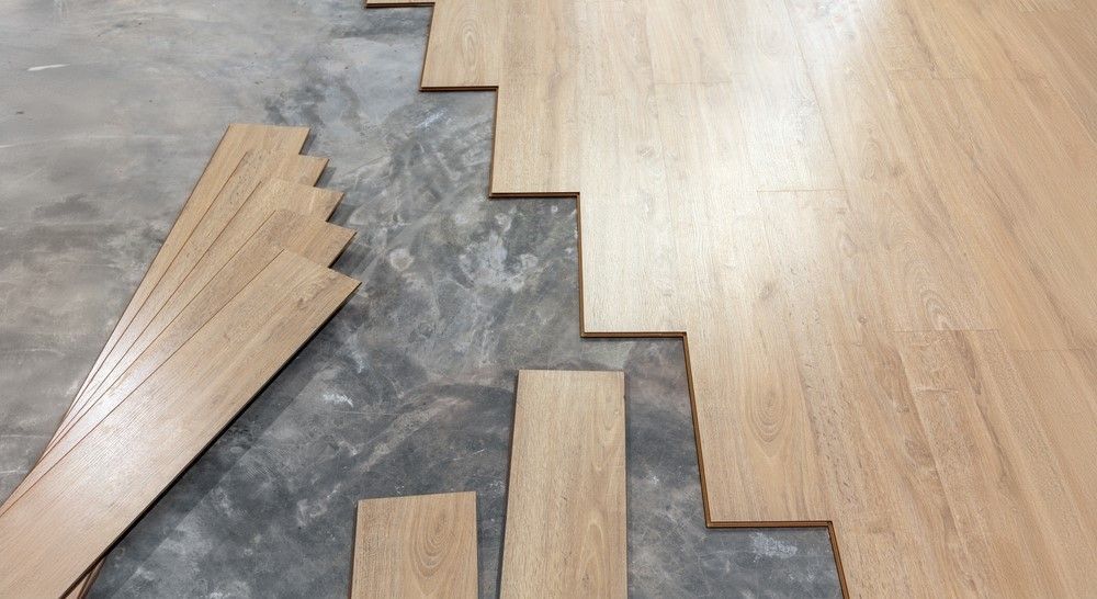 Light brown wood flooring planks being installed on a gray concrete surface.