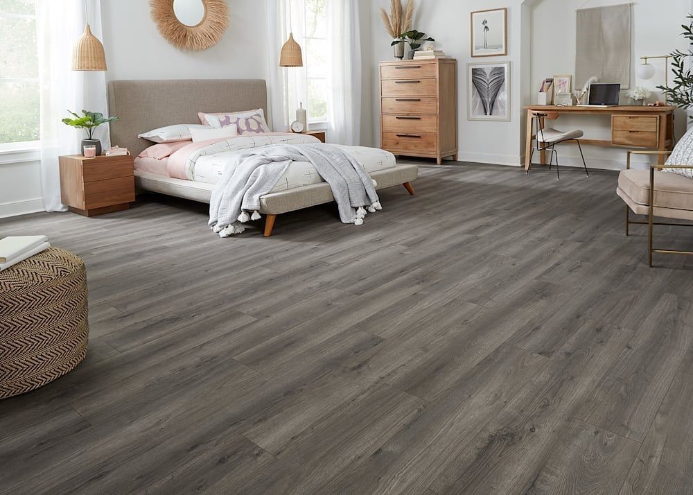 Bedroom with gray wood-look flooring, bed, dresser, desk, and neutral decor.