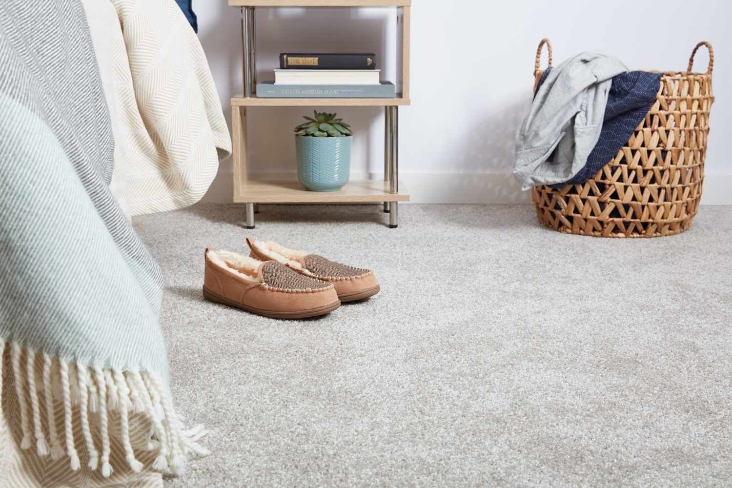 Cozy bedroom with slippers, blanket, basket of clothes, and small shelving unit.