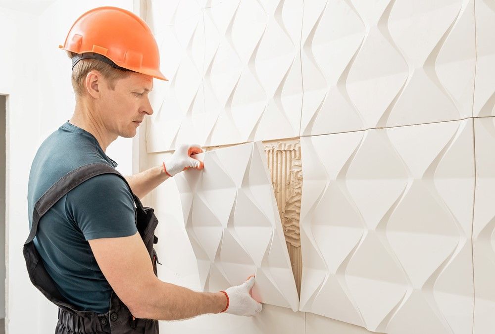Construction worker installing textured white wall panels. Orange hard hat, gloves.
