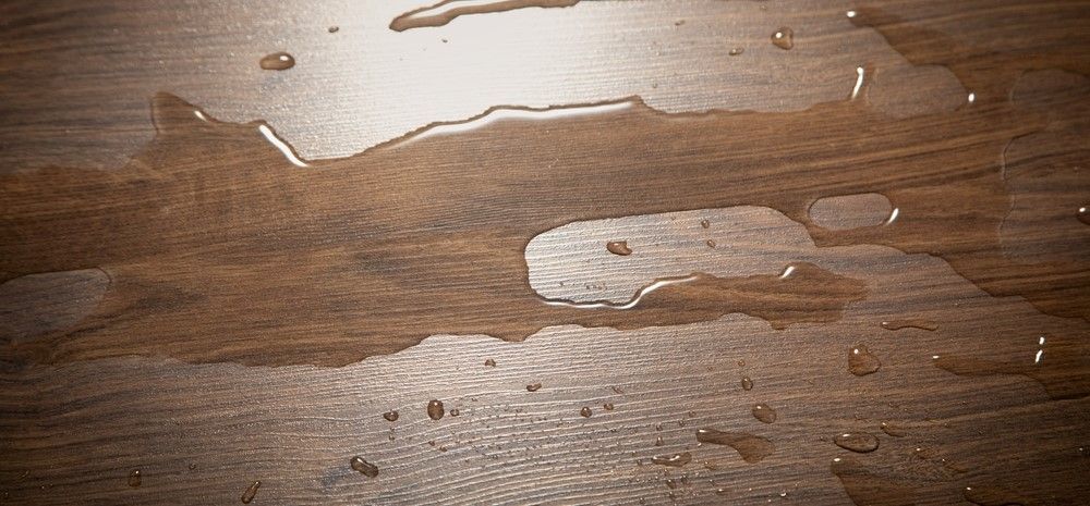 Water droplets and spilled liquid on a brown wooden surface.