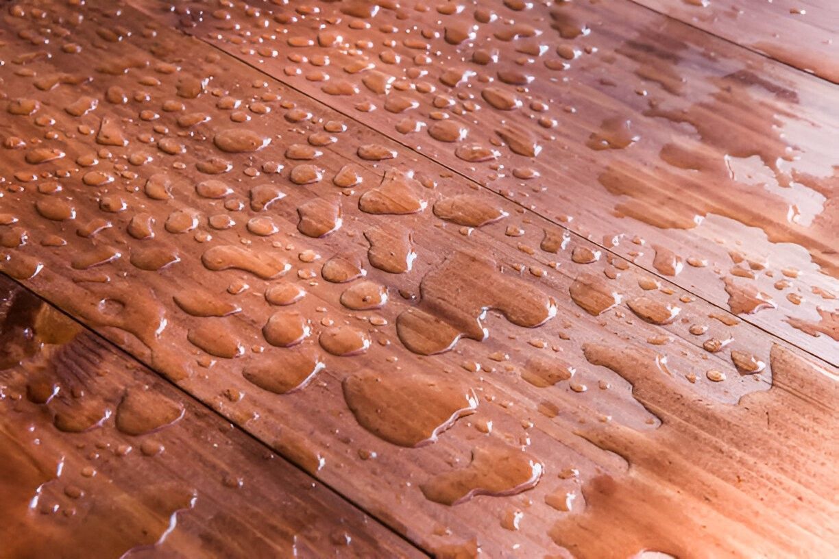 Water droplets on a shiny, wooden floor.