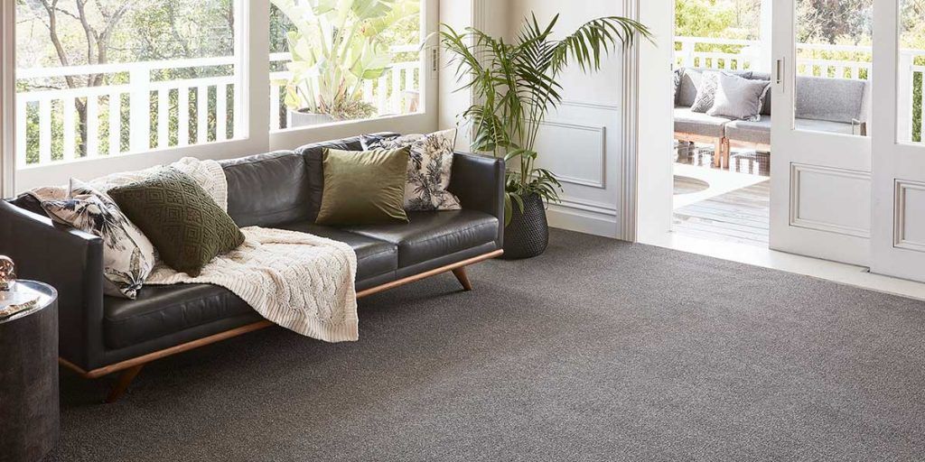 Living room with dark leather sofa, green pillows, gray carpet, and large windows.