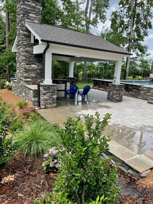 Outdoor covered patio with stone fireplace, bar, seating, and landscaping.
