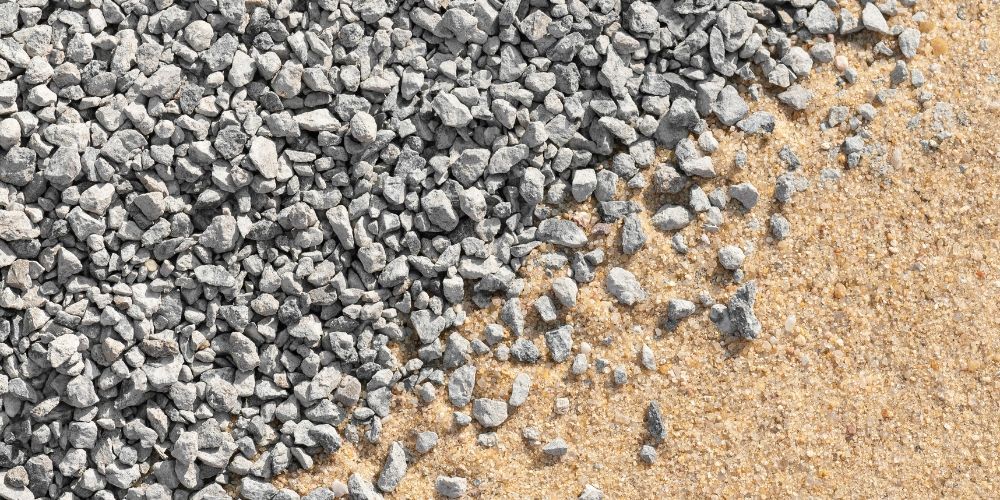 Gray gravel and tan sand meeting in a close-up textured ground surface