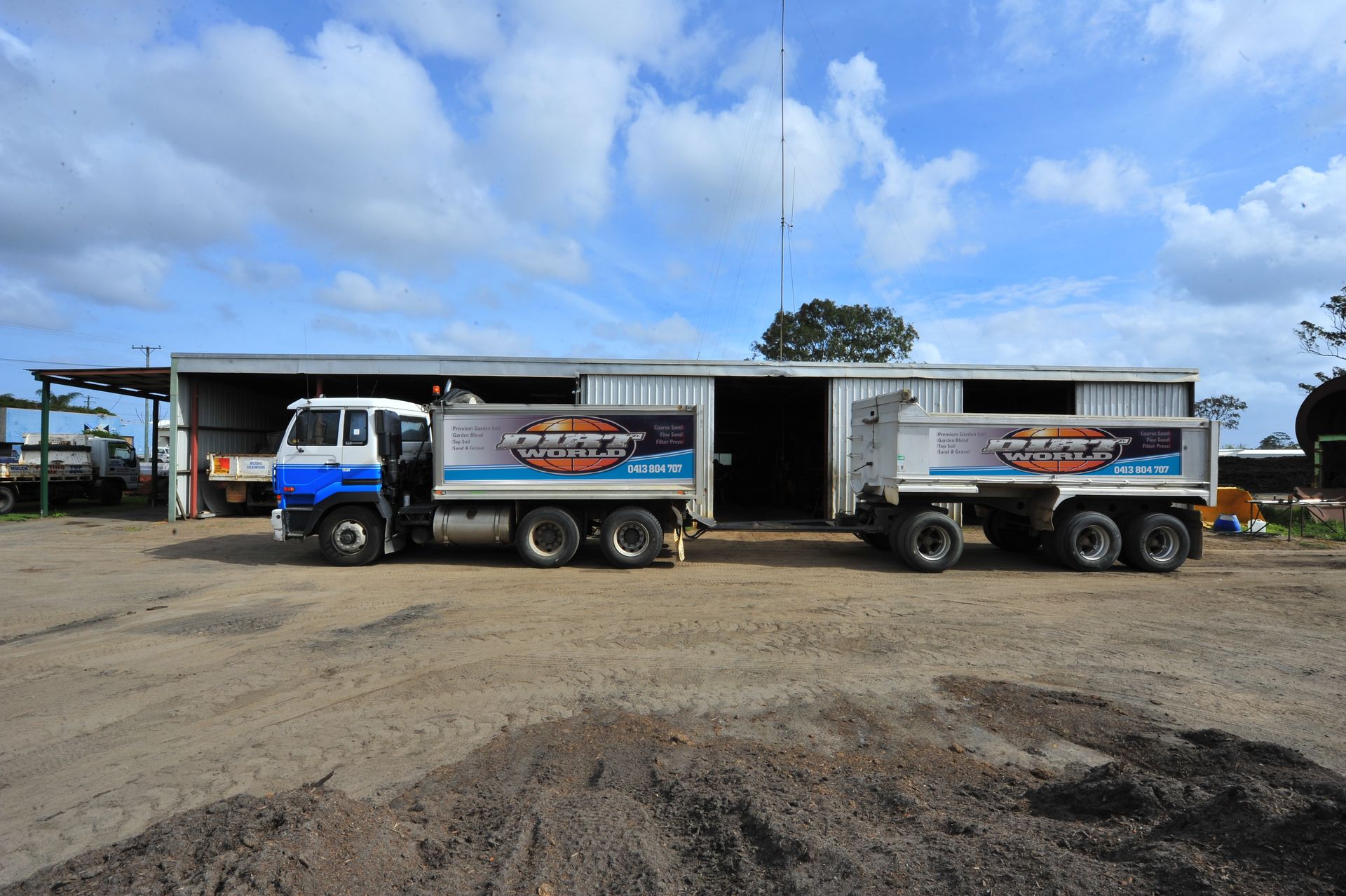 Two blue-and-white trucks parked on a dirt lot under a cloudy sky.