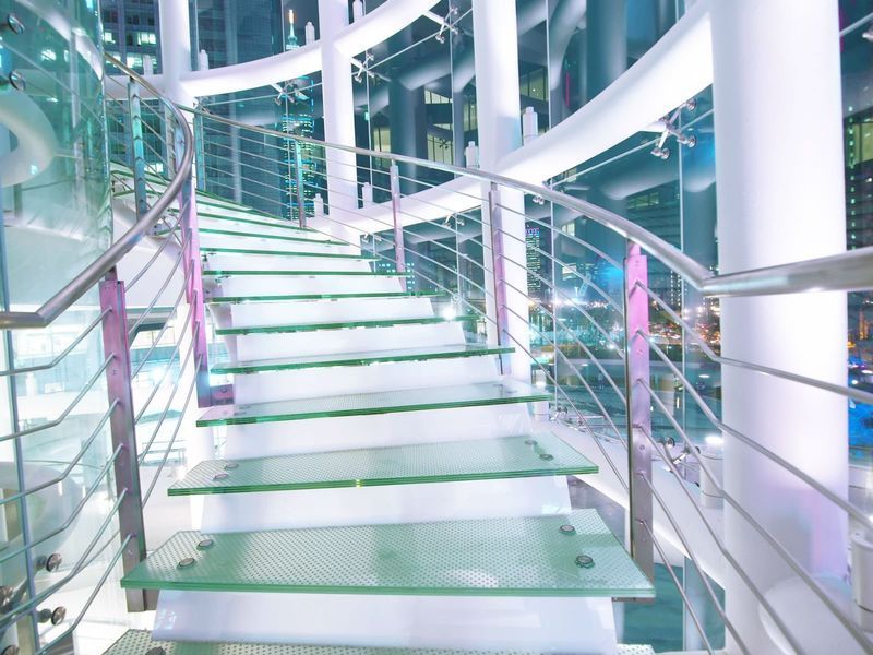 Una moderna scala a chiocciola con gradini in vetro verde traslucido, ringhiere in acciaio inossidabile e colonne di sostegno bianche.
