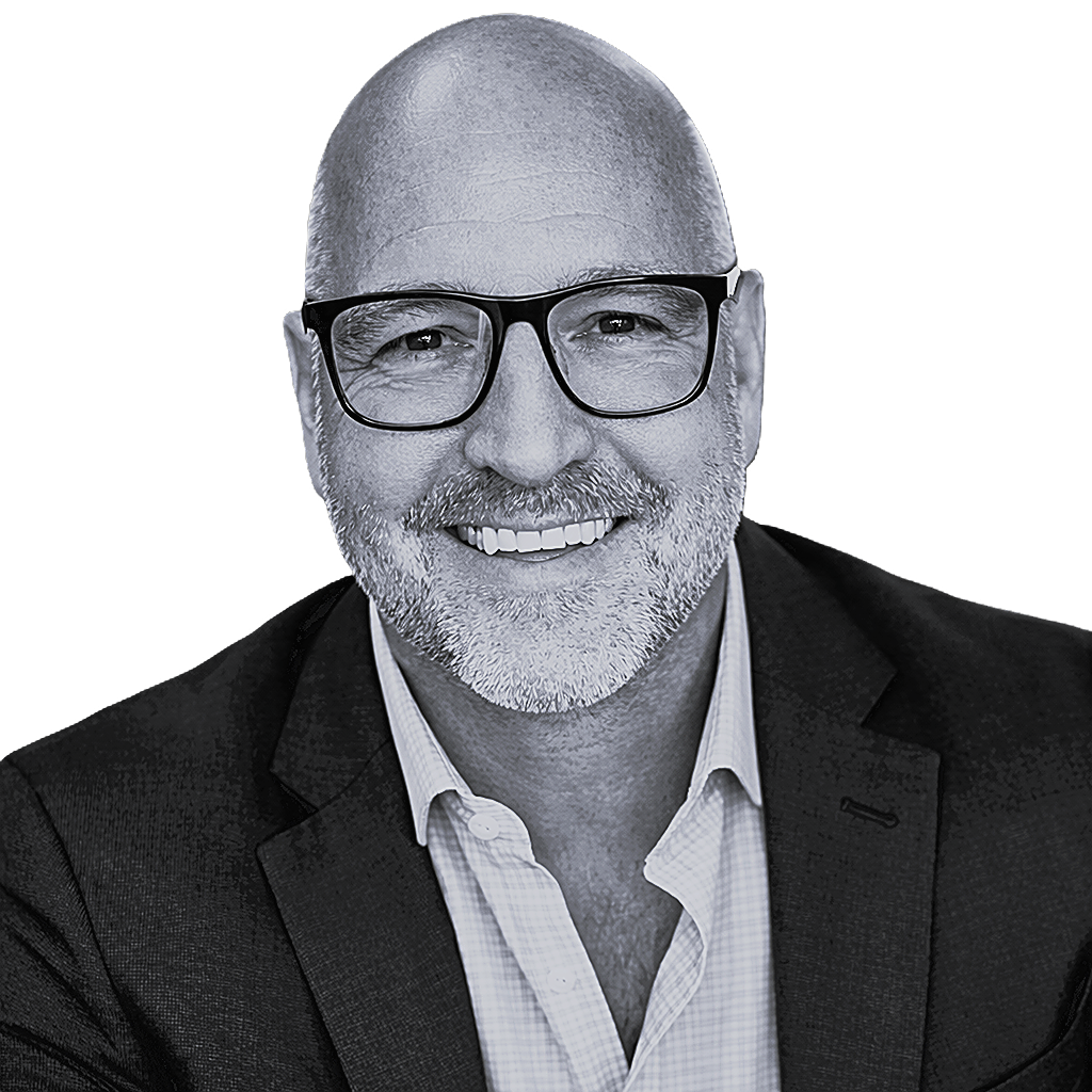 A bald man wearing glasses and a plaid shirt is smiling.