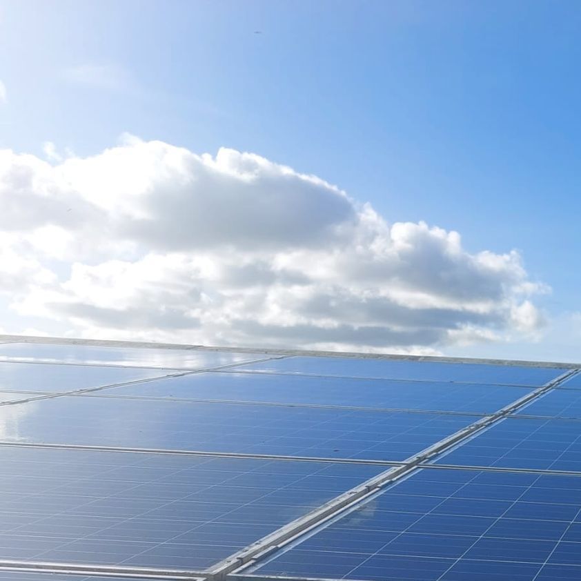 A row of solar panels against a blue sky with clouds.