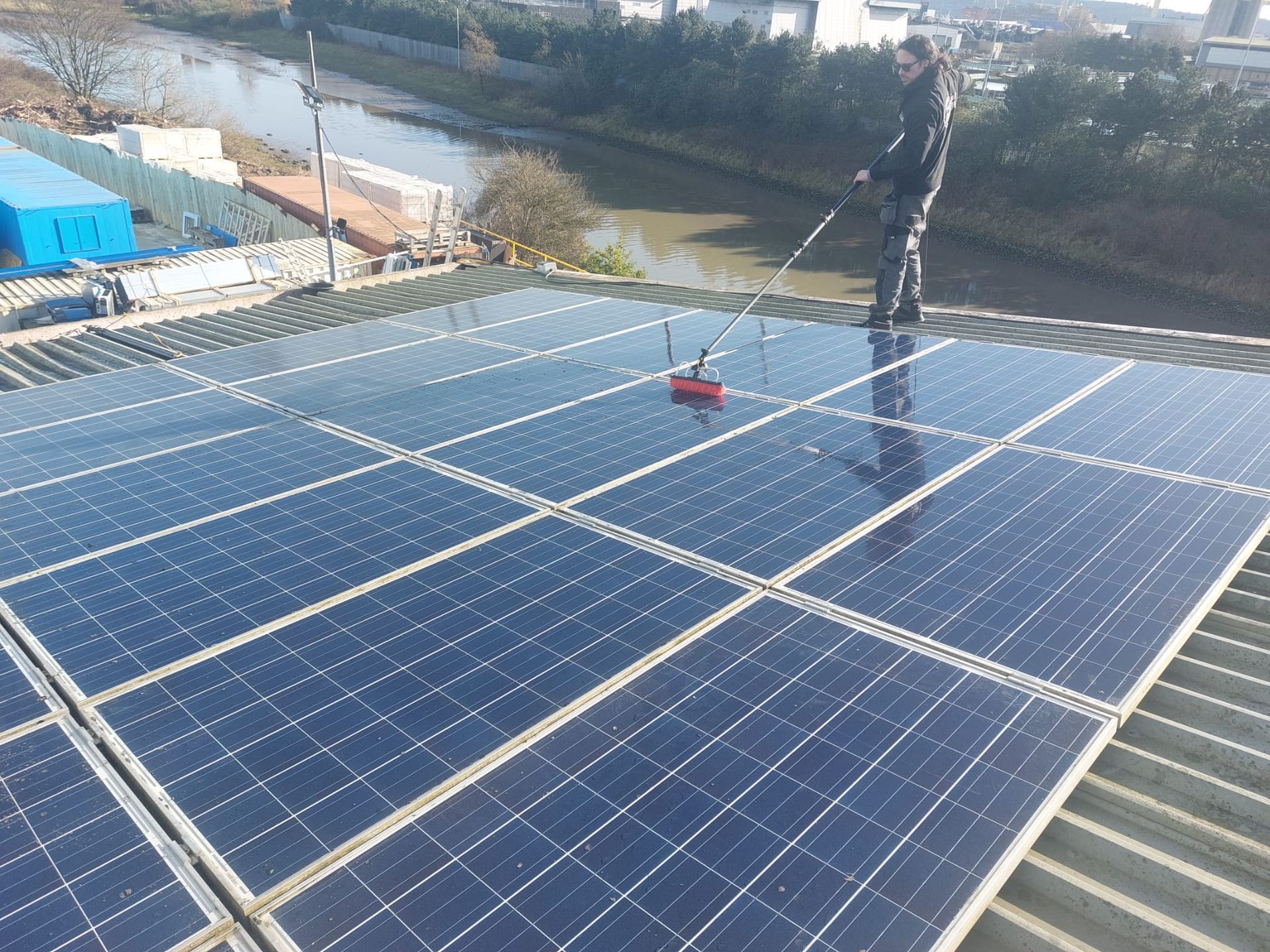 A man is cleaning solar panels on the roof of a building.