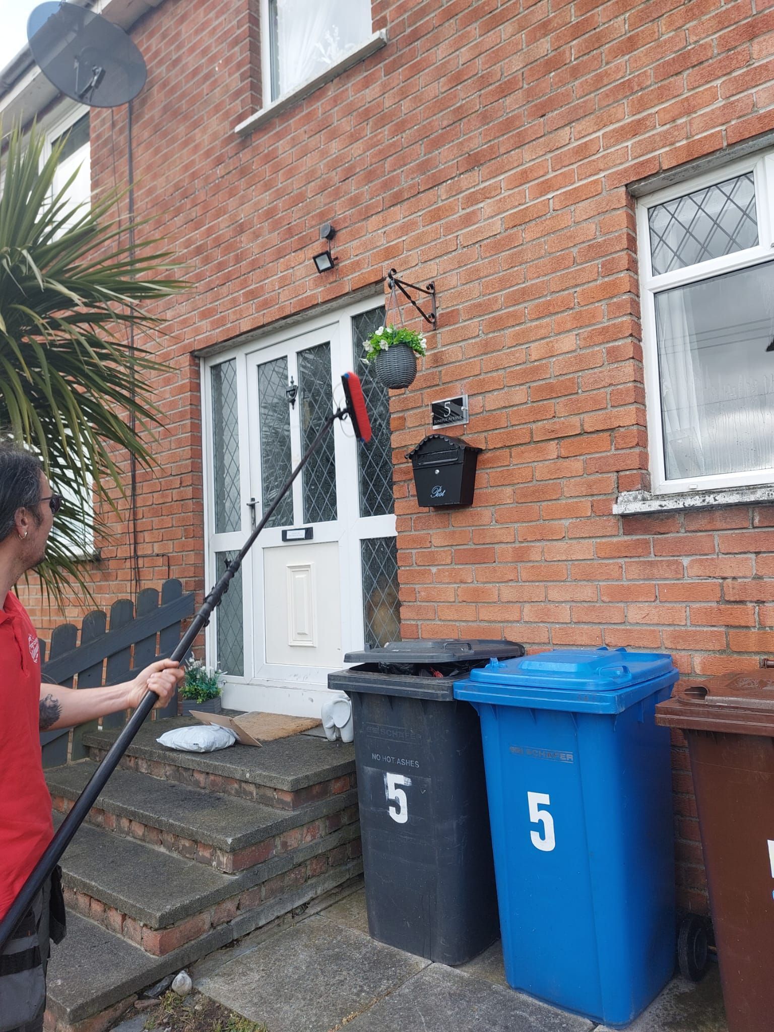 A man is cleaning the front of a brick house with a mop.