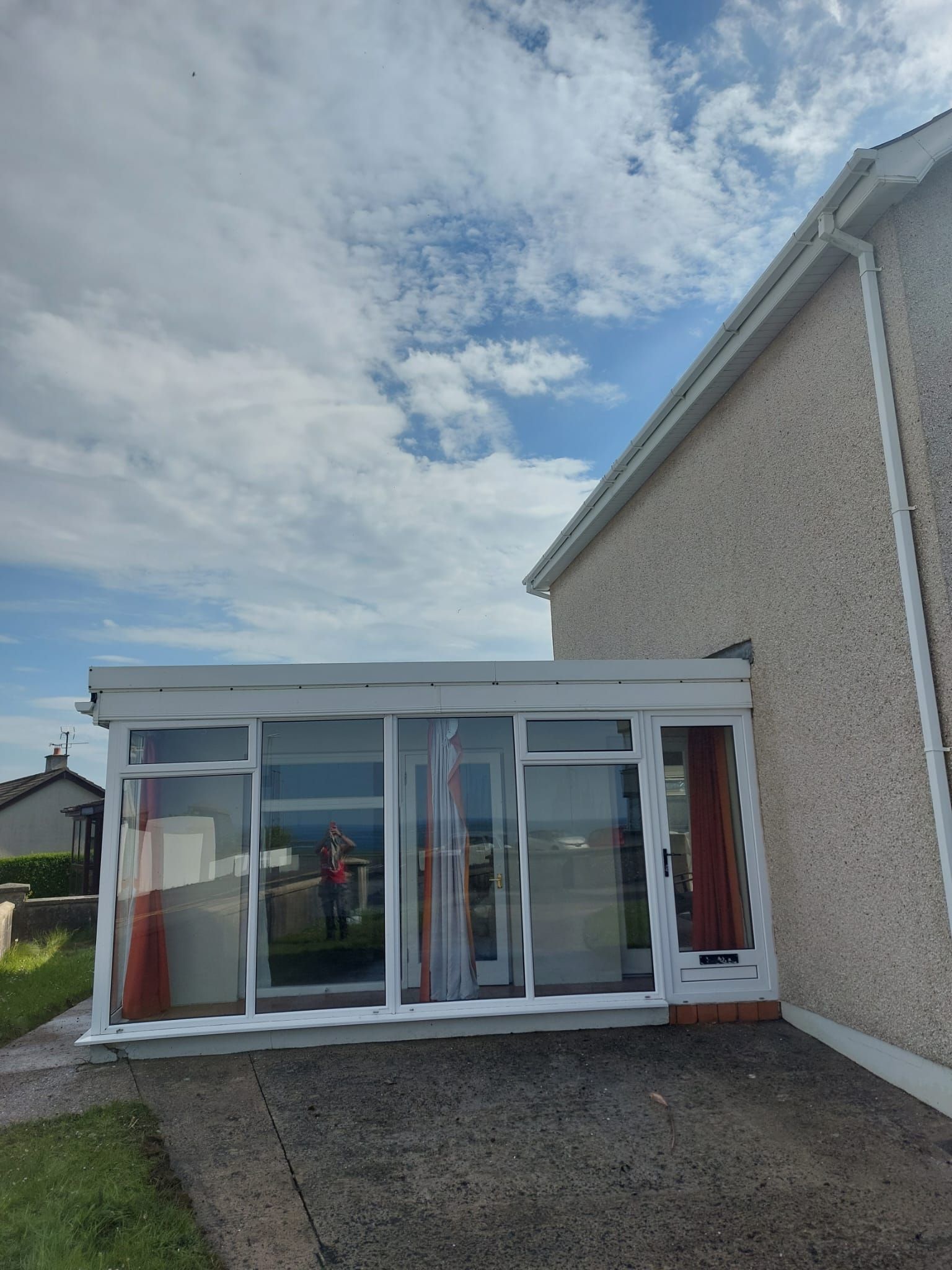 A house with a conservatory attached to it and a blue sky in the background.