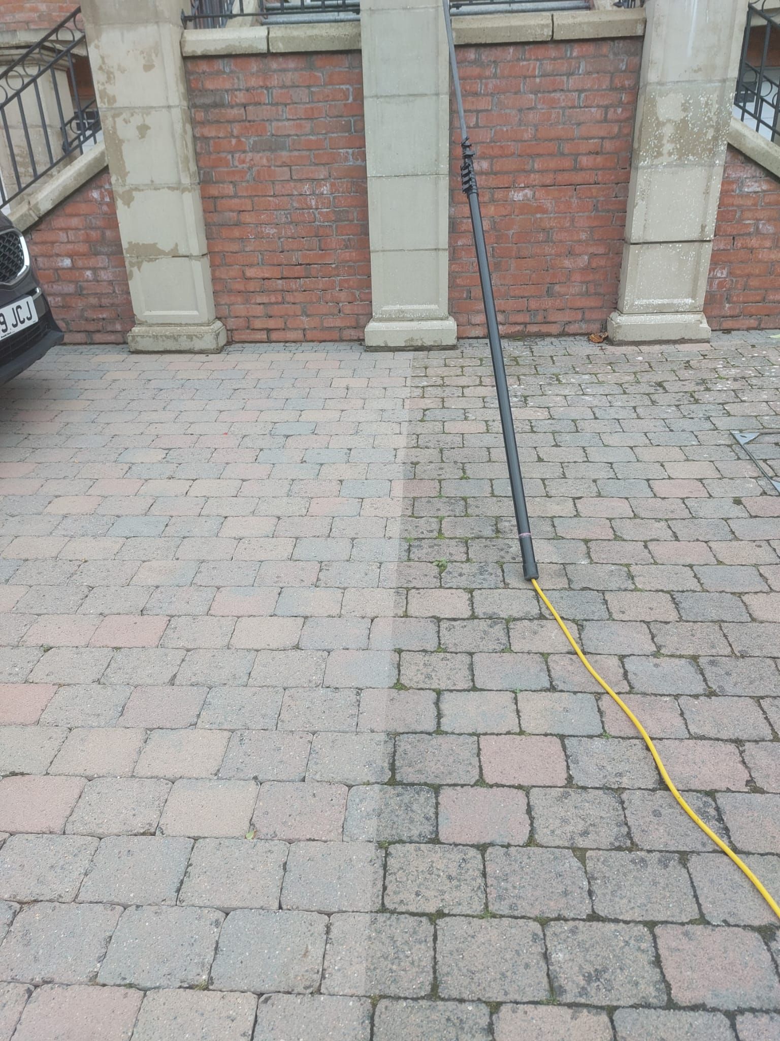 A car is parked on a brick driveway next to a brick wall.