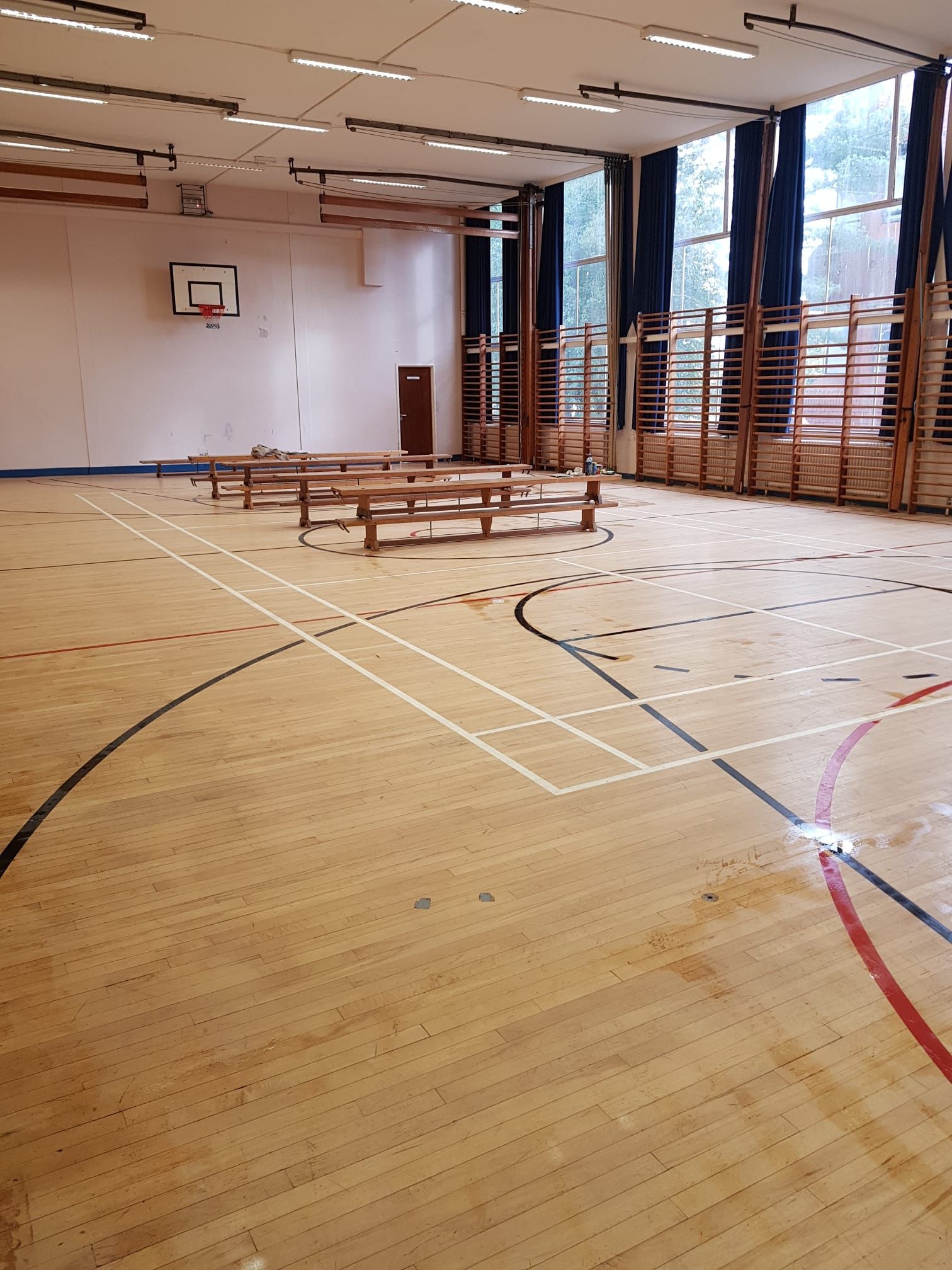 An empty gym with a wooden floor and a basketball hoop.