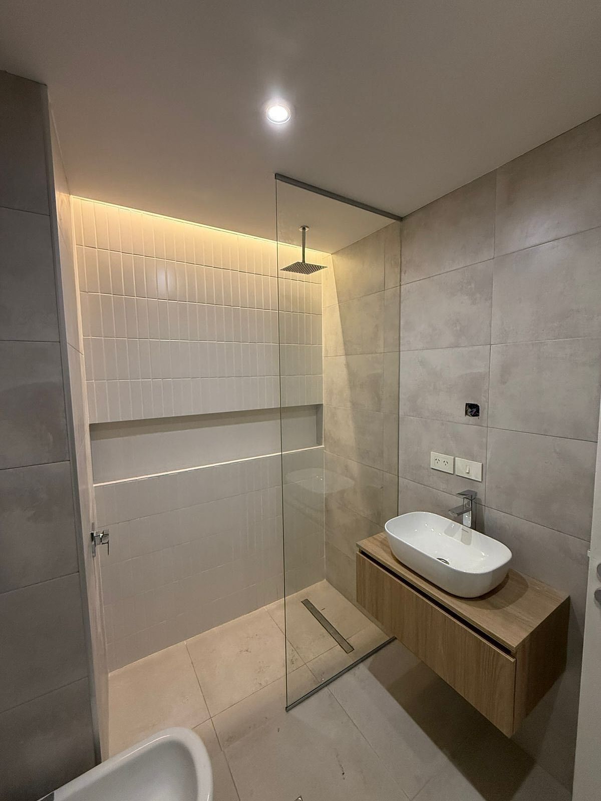 Baño moderno con ducha de cristal, tocador flotante y azulejos de colores claros.