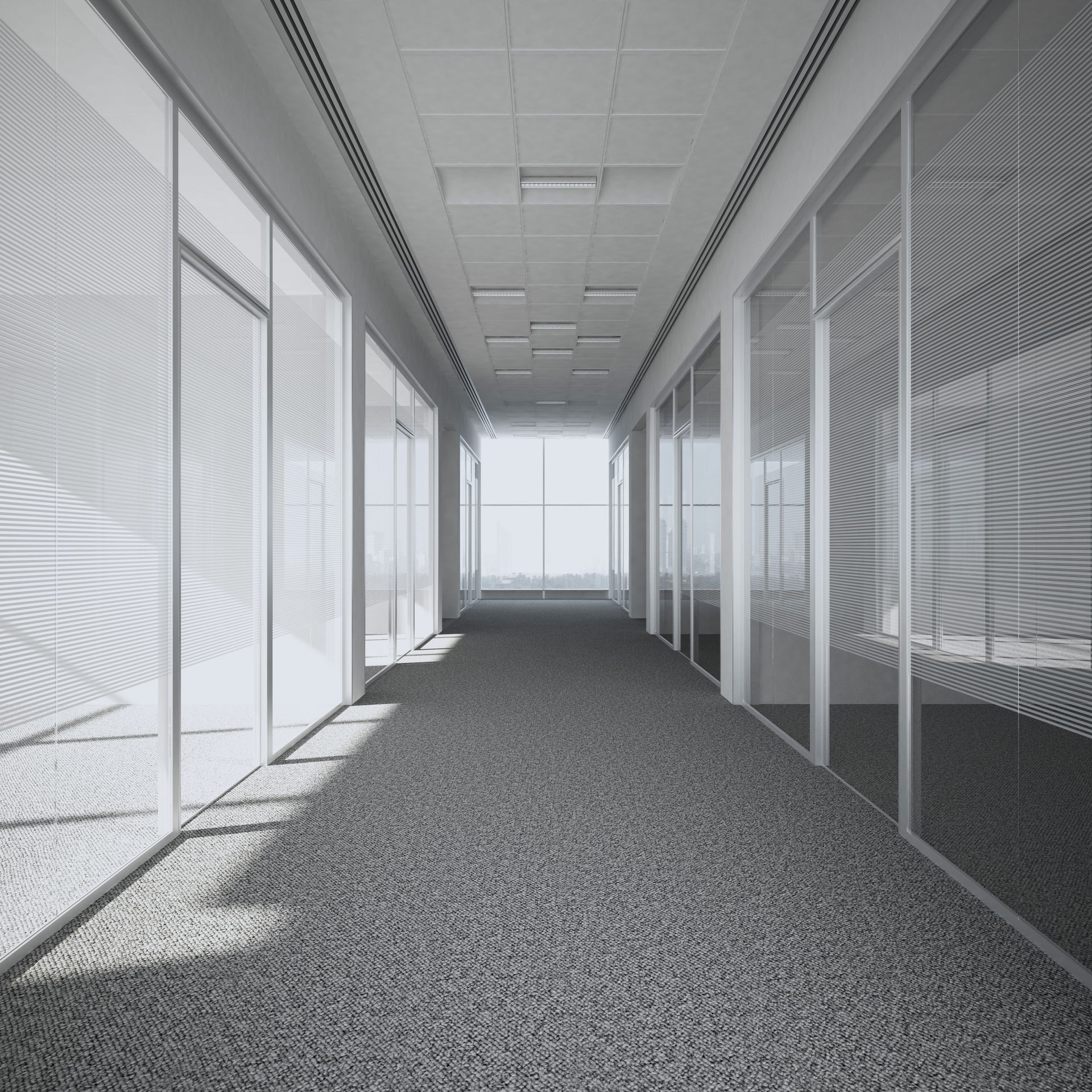 Pasillo con oficinas con paredes de cristal, alfombra gris y luz brillante al final.