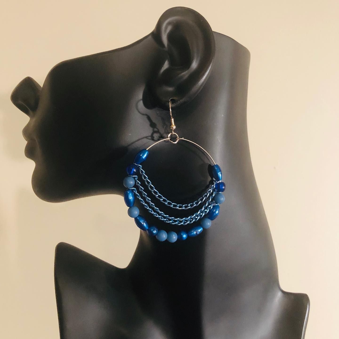 Blue beaded hoop earrings displayed on a black mannequin ear.