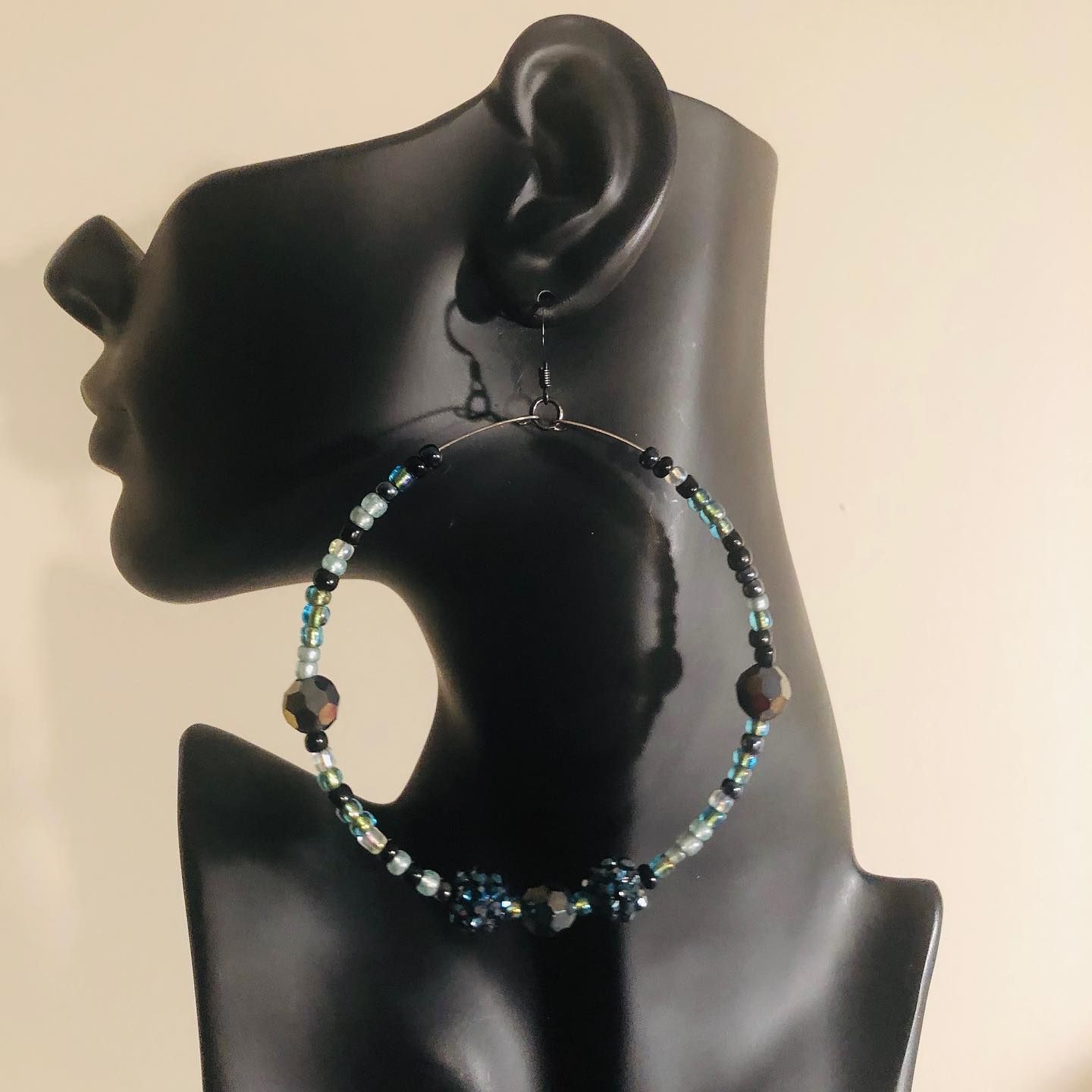 Beaded hoop earrings with black, green, and dark blue beads on a black mannequin head.