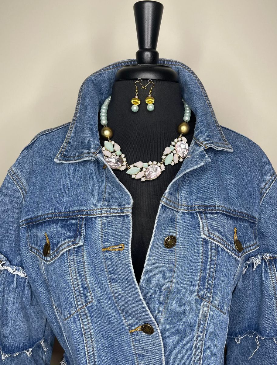 Denim jacket, necklace, and earrings on a mannequin. The jacket is blue with gold buttons.