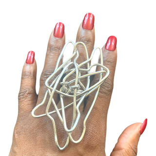 A hand wearing a large, silver, abstract-shaped ring, with bright red nails, against a white background.