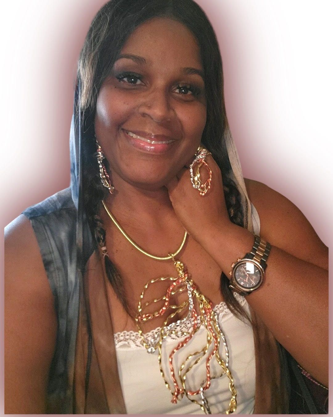 Woman smiles, wearing jewelry, tank top, and a watch. Features long, dark hair and light makeup.
