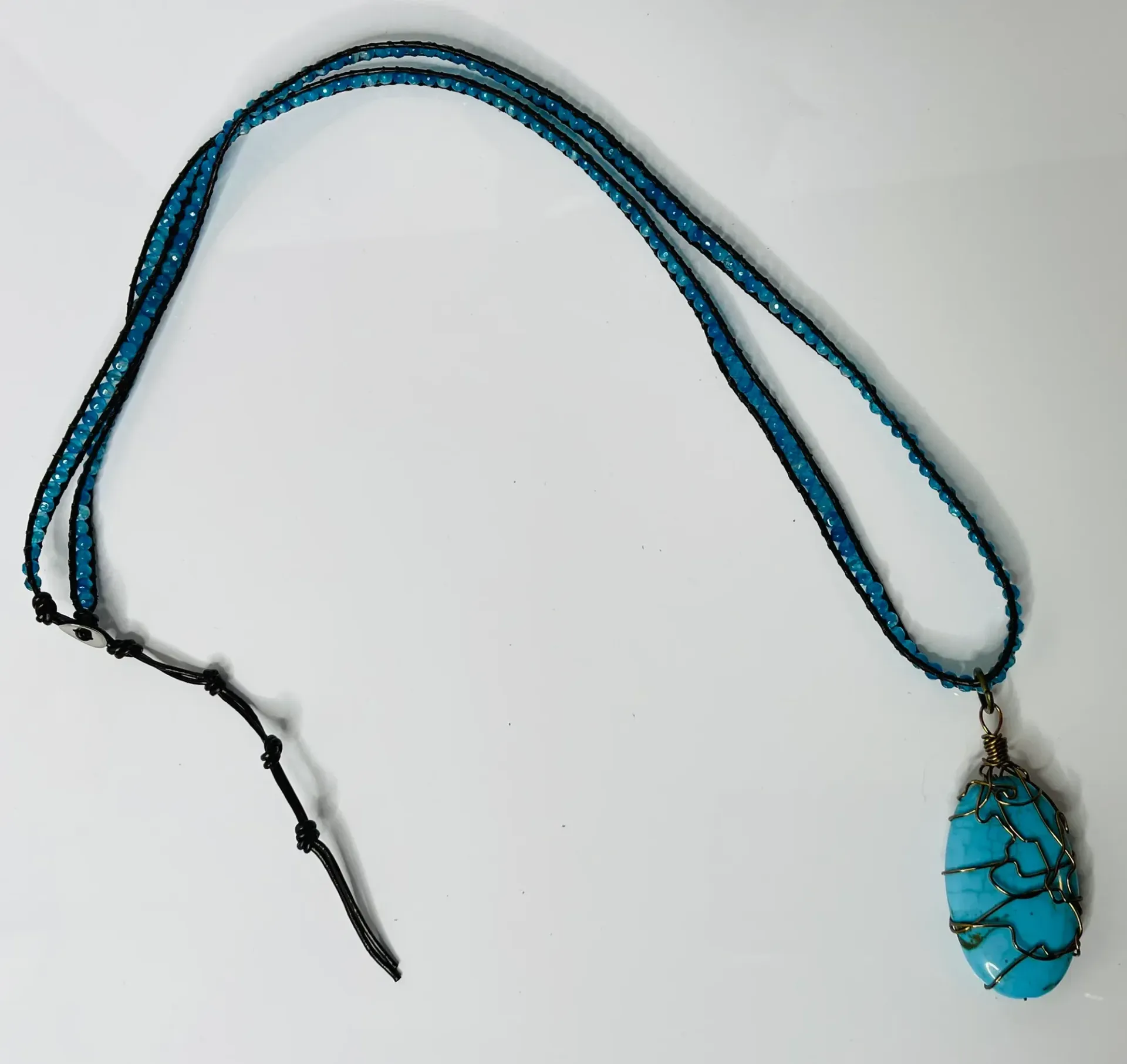 Blue beaded necklace with a turquoise pendant, on a white surface.