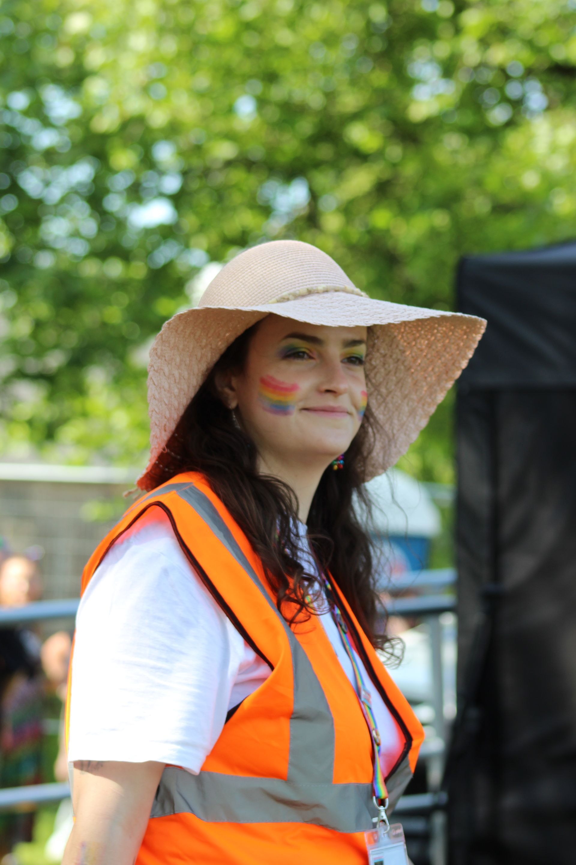 A volunteer wearing a sun hat with rainbow face paint.