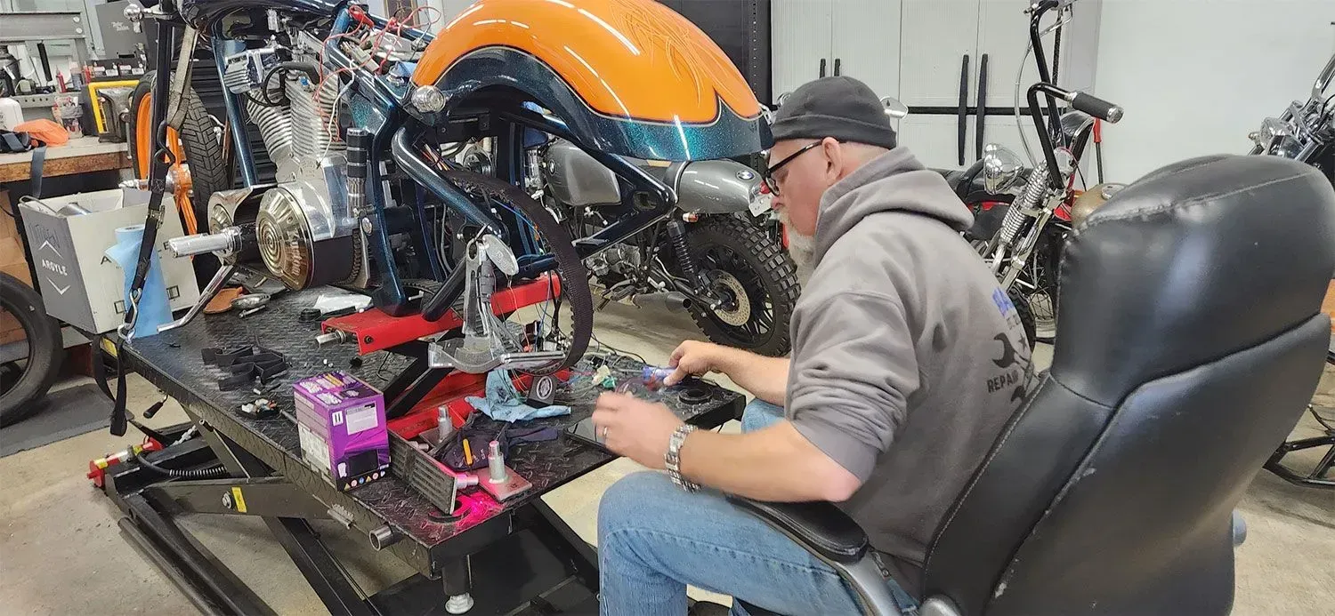 A man is sitting in a chair working on a motorcycle in a garage.