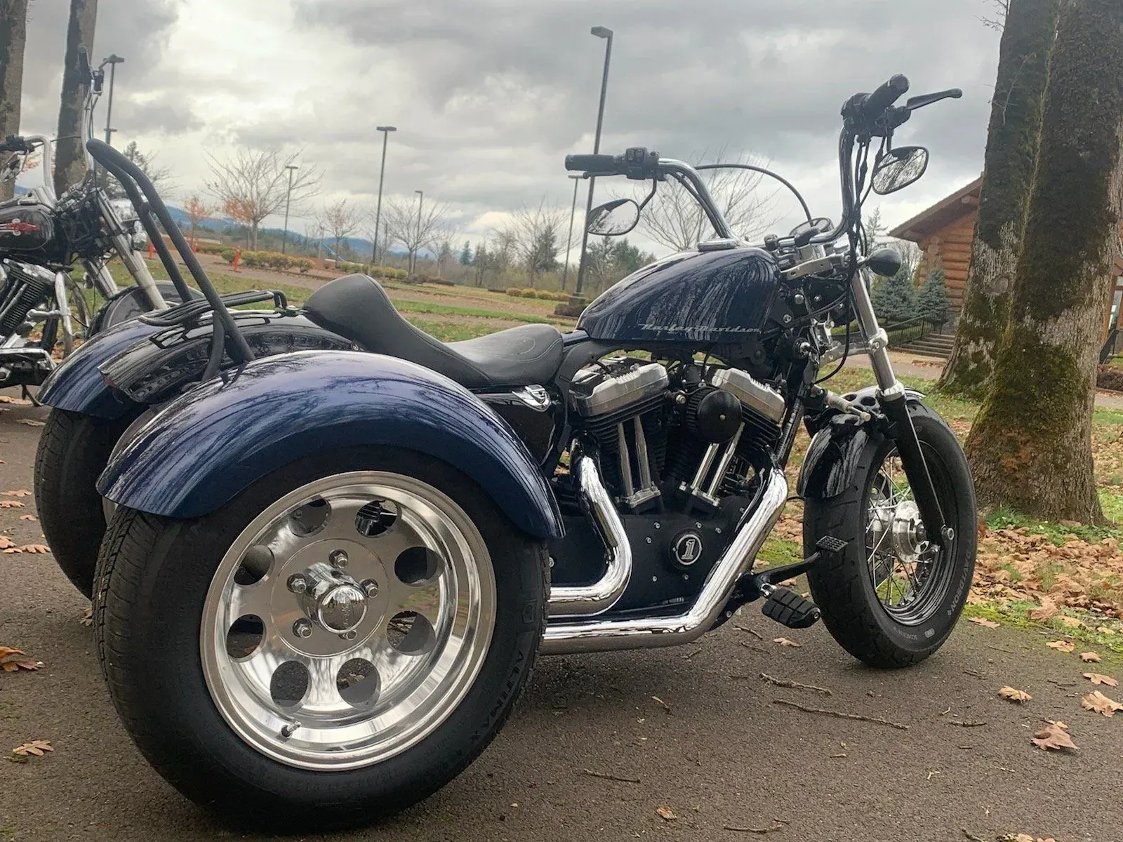 A blue motorcycle with three wheels is parked on the side of the road.