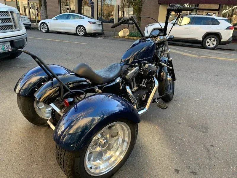 A blue motorcycle with three wheels is parked on the side of the road.