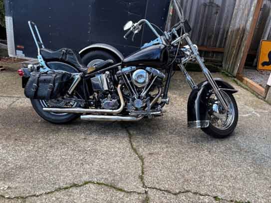 A black motorcycle is parked in a driveway next to a trailer.