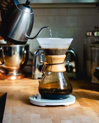 Pour-over coffee brewing with a kettle pouring water into a Chemex on a wooden counter