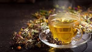 Glass cup of herbal tea on a saucer beside loose dried flowers and herbs