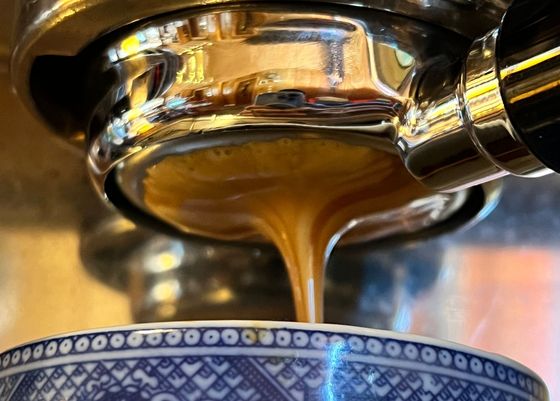 Coffee pouring from an espresso machine into a blue patterned cup