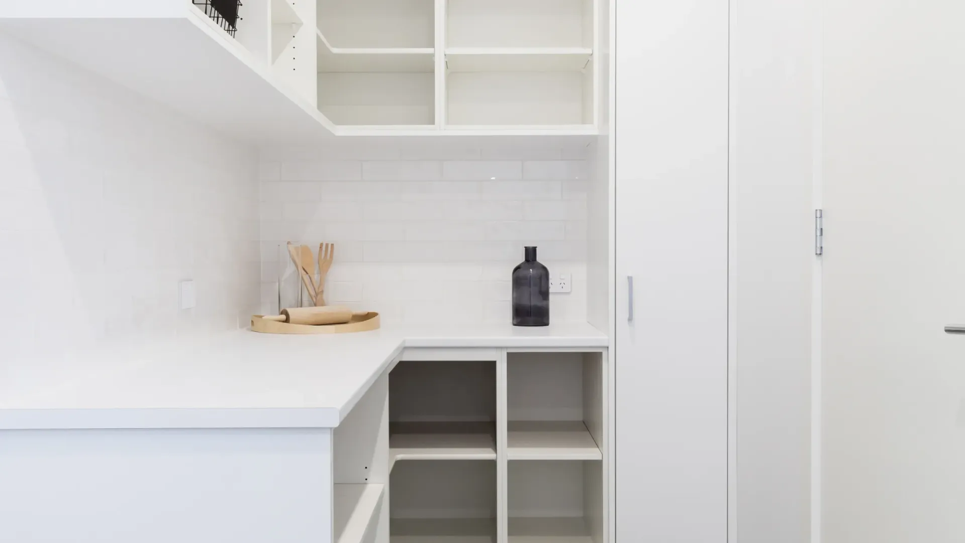 A butler's pantry with white cabinets and shelves and a bottle on the counter.