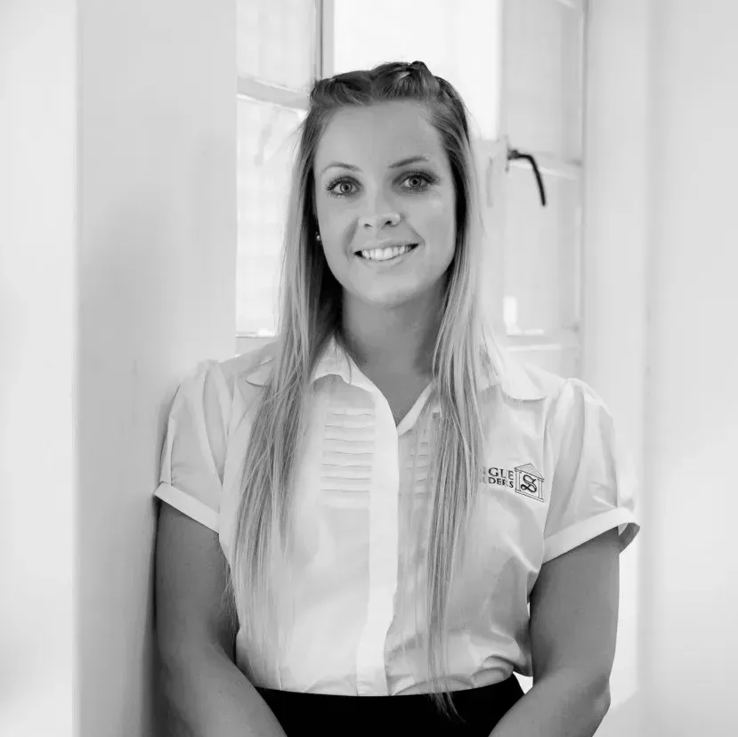 A woman in a white shirt is leaning against a wall and smiling.