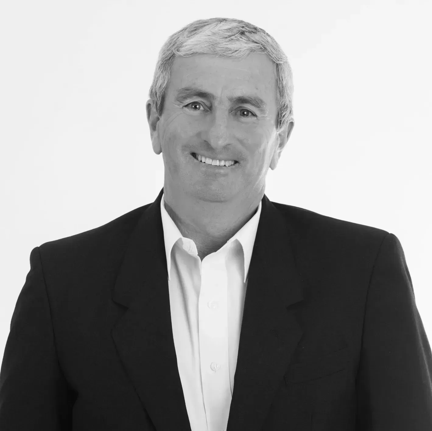 A man in a suit and white shirt is smiling in a black and white photo.