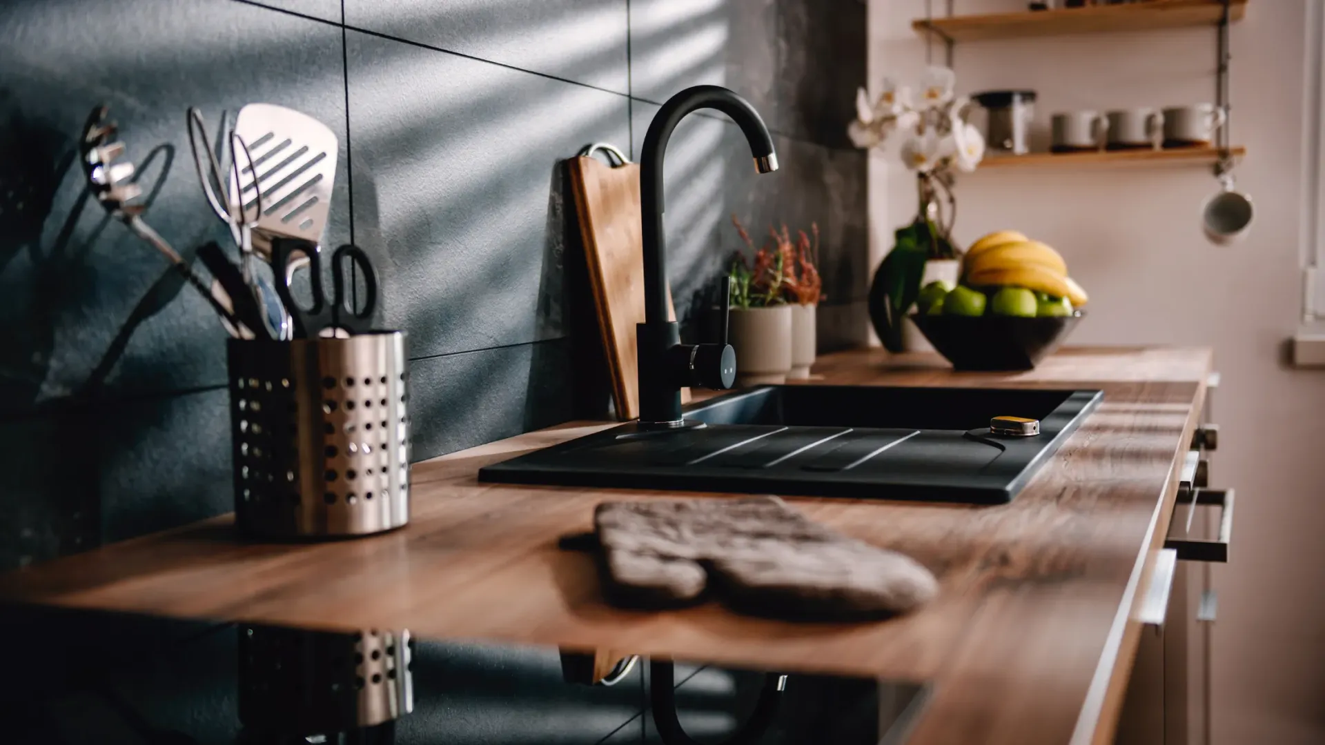 A kitchen with a sink , stove , and utensils on the counter.