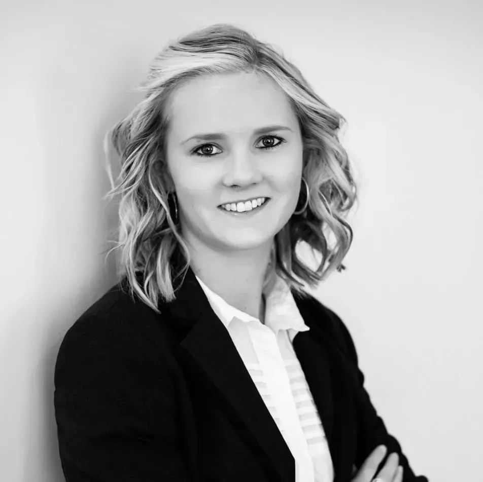 A woman in a suit and white shirt is smiling in a black and white photo.