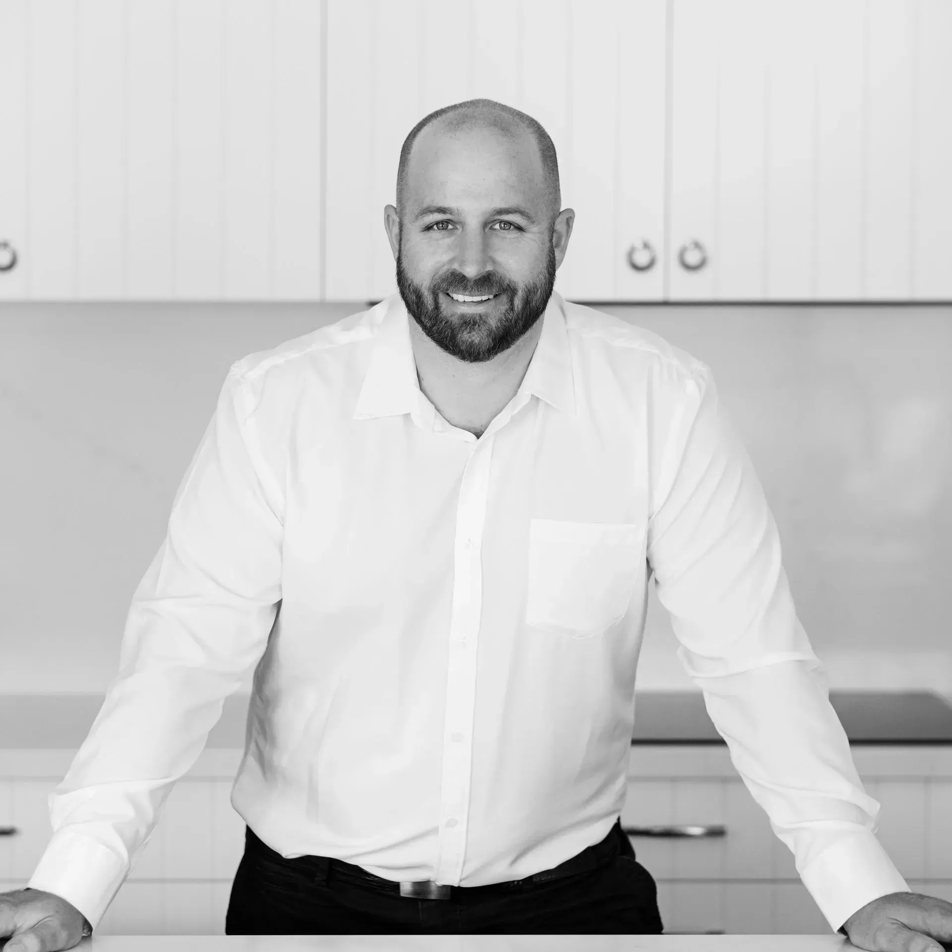 A man with a beard is leaning on a counter in a kitchen.