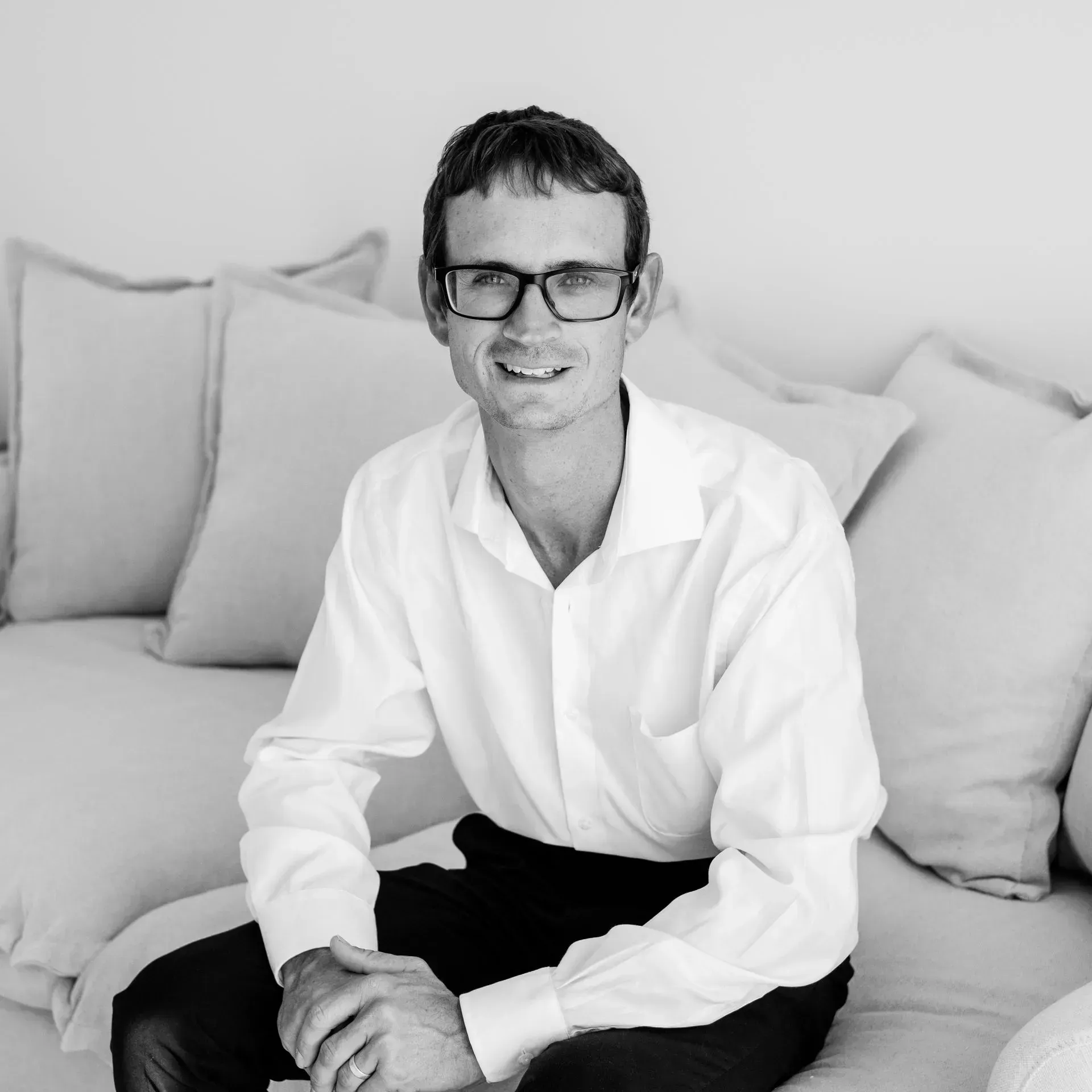 A man wearing glasses and a white shirt is sitting on a couch