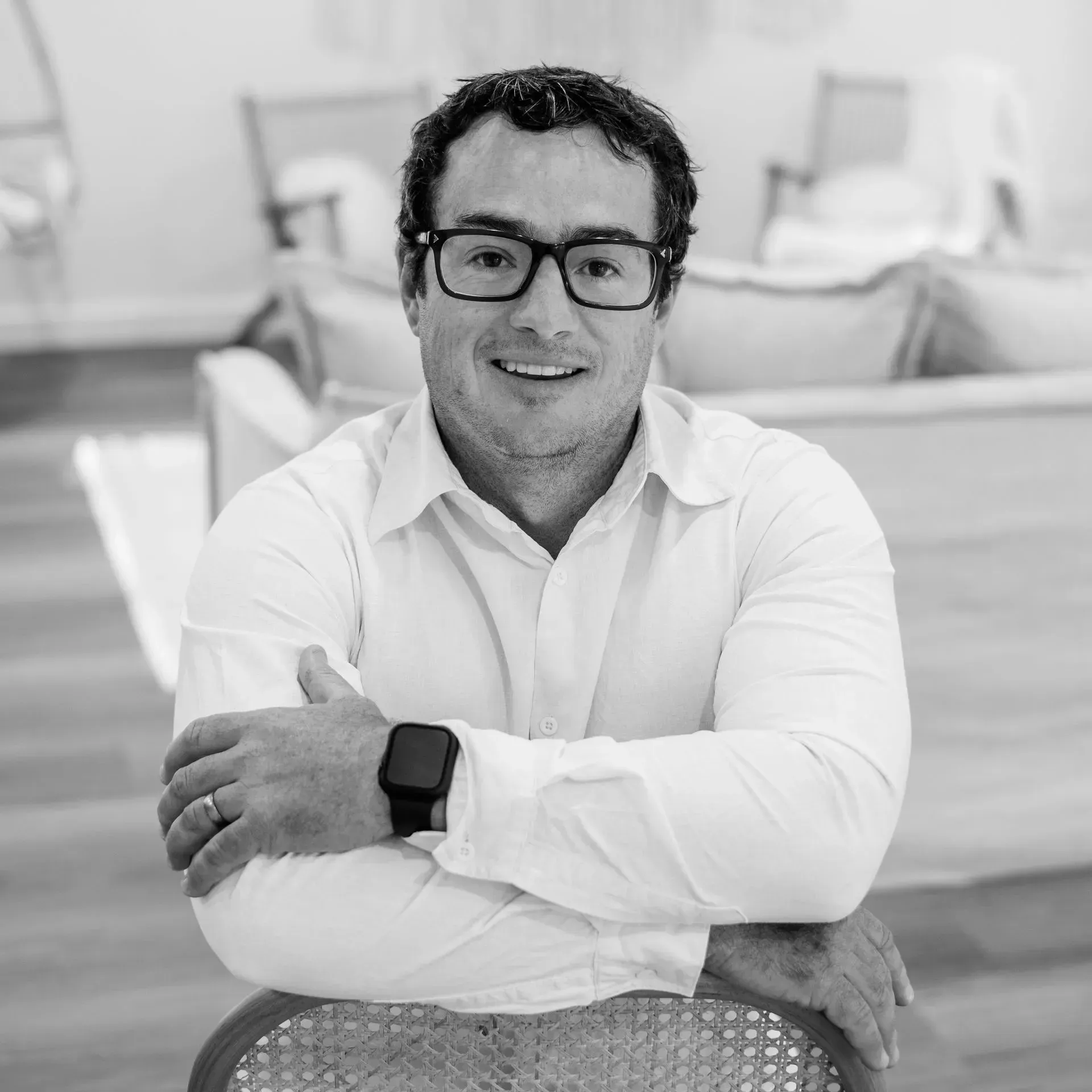 A man wearing glasses and a watch is sitting in a chair with his arms crossed.