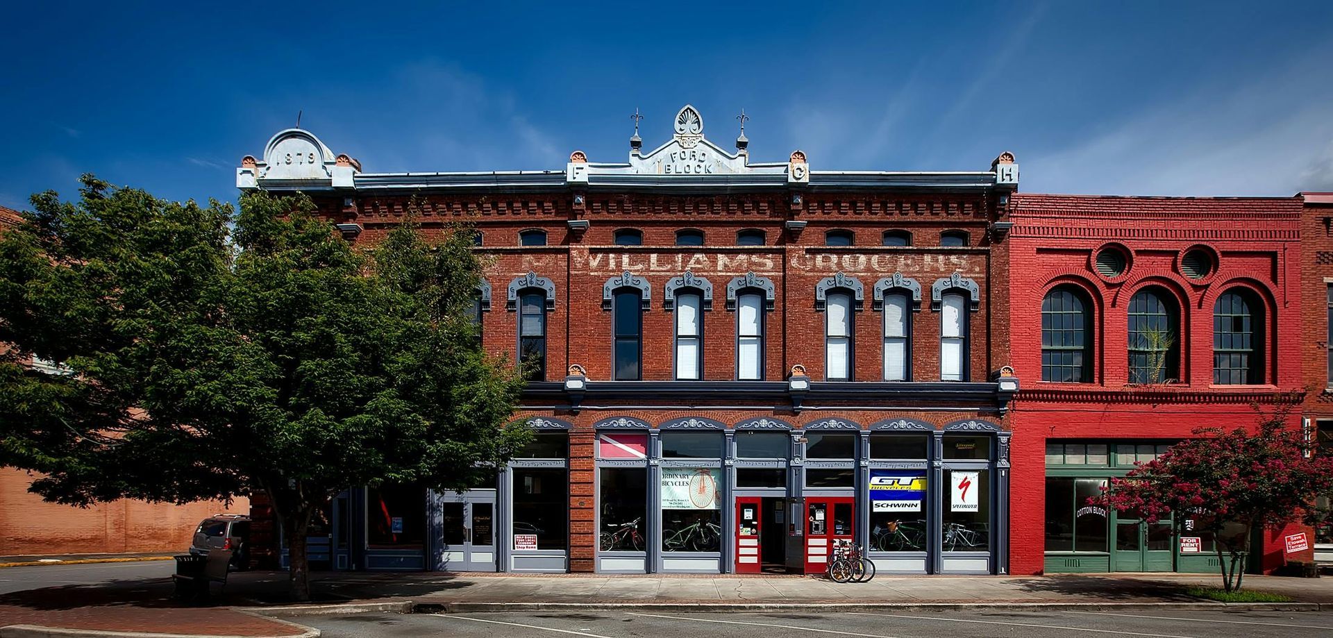 Historic small-town main street with brick buildings, colorful shop awnings, and trees lining the sidewalk.