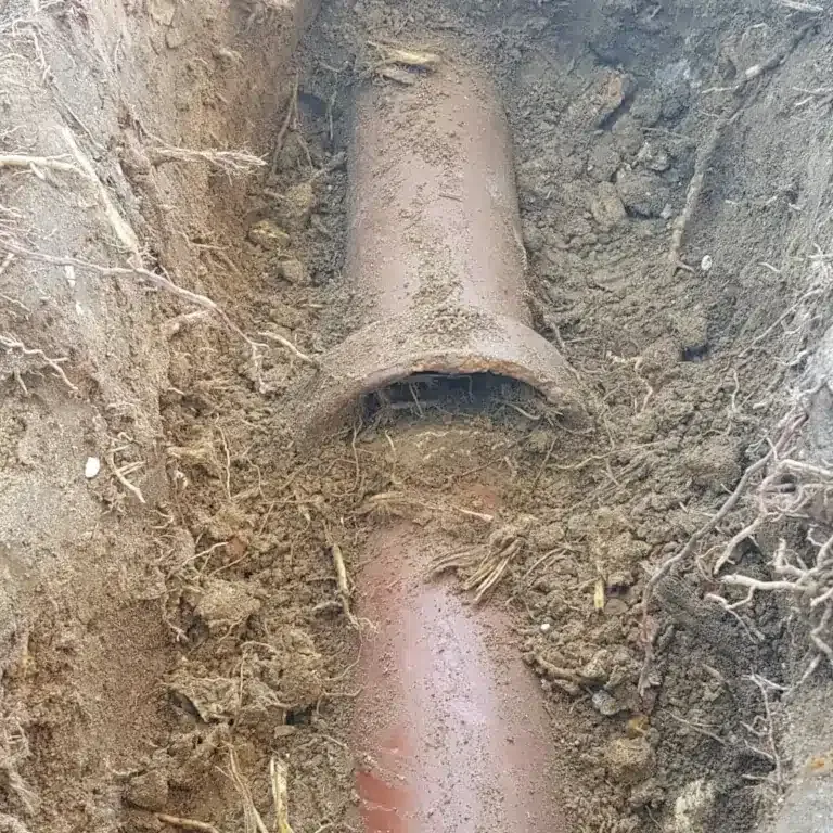 A brown clay sewage pipe joint exposed in a narrow, dirt-filled trench.