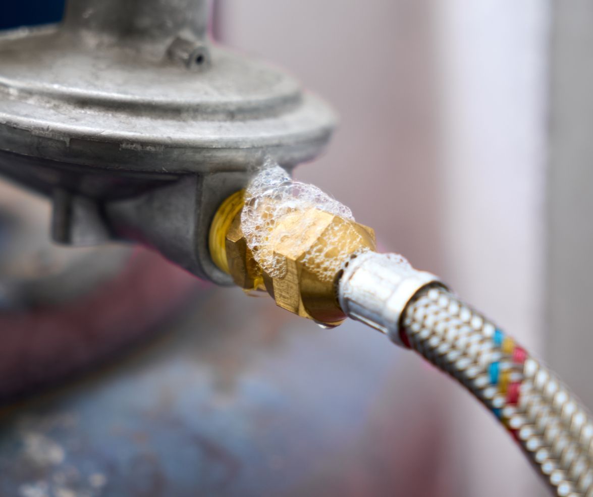 Bubbles forming at a brass hose connection on a propane regulator, indicating a dangerous gas leak.