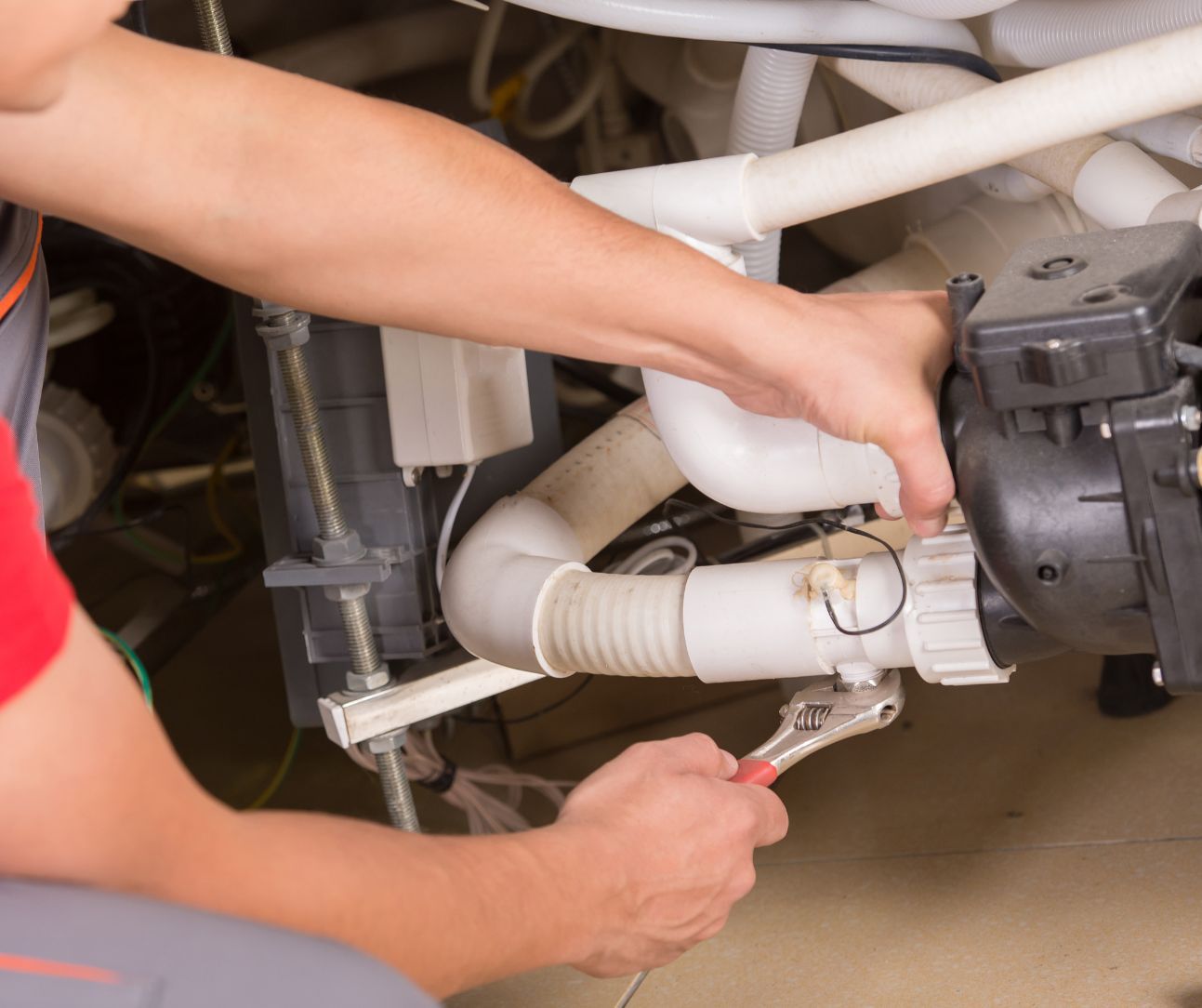 A technician uses an adjustable wrench to tighten a fitting on white PVC plumbing connected to a pump.