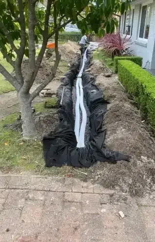 A long drainage trench lined with black fabric and gravel with white corrugated piping installed in a front garden.