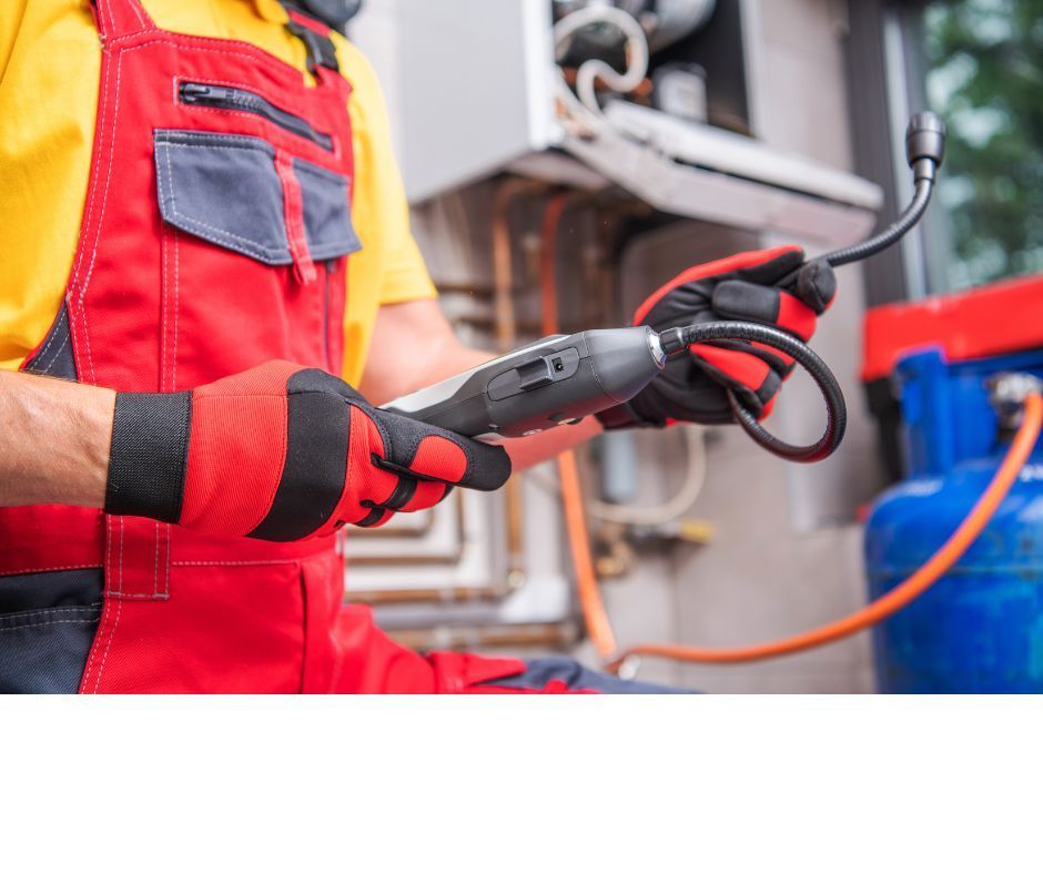 A technician in red and yellow work coveralls uses a gas leak detector near a blue propane tank and heating equipment.